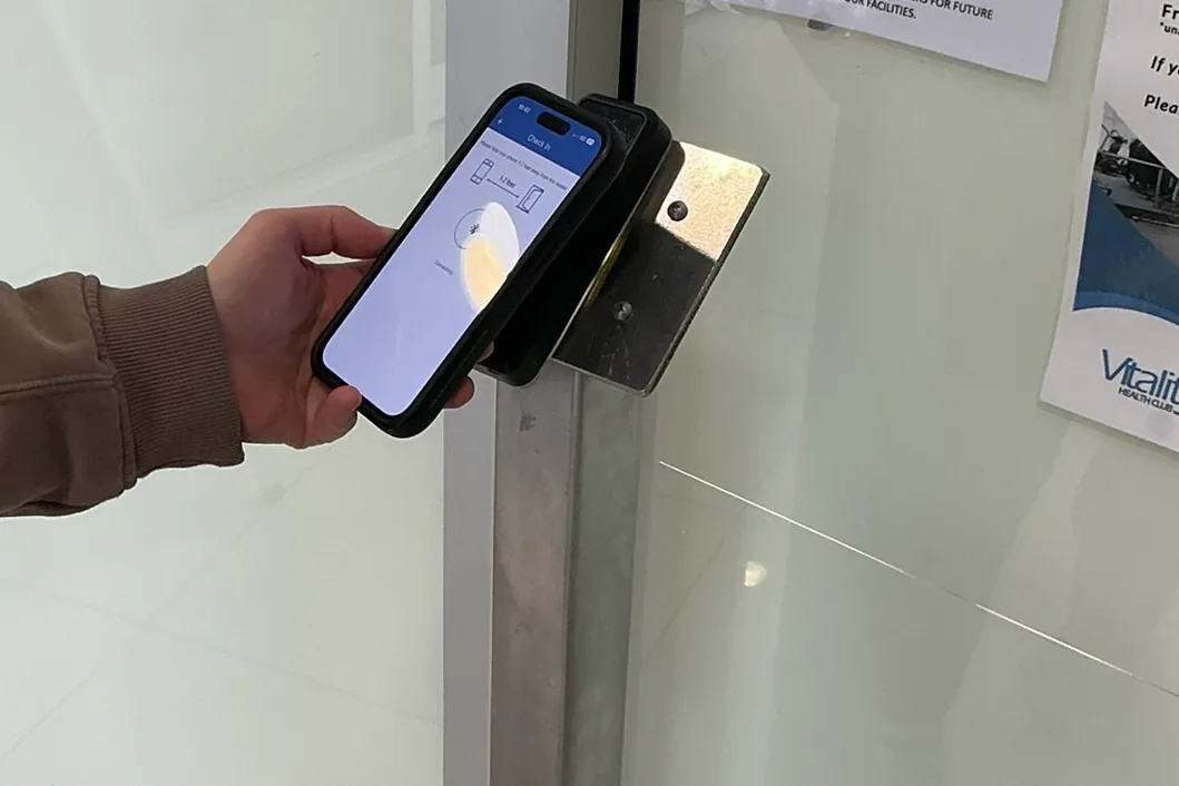 A hand holding a phone against the card reader beside the club door, the membership app open on screen
