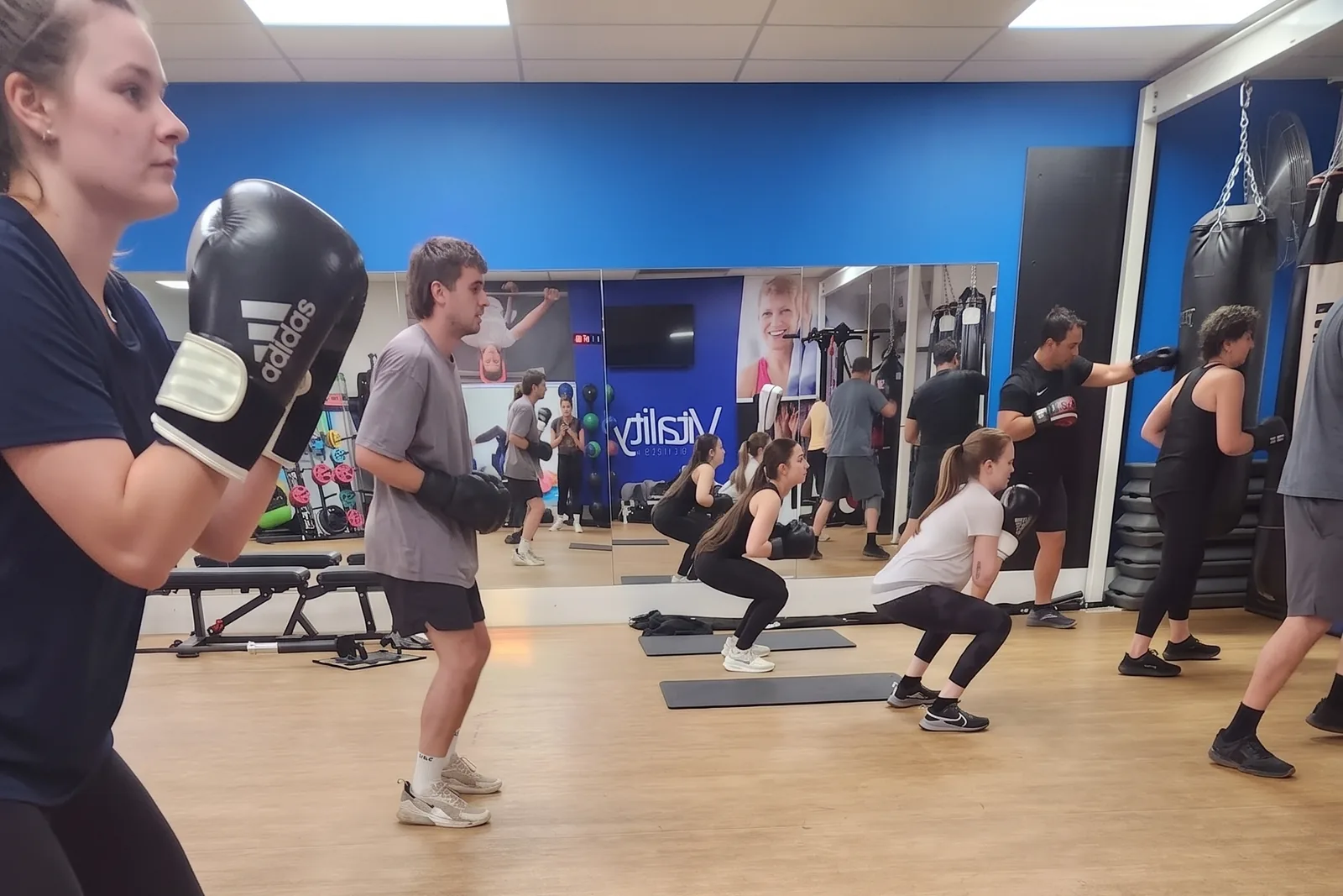A boxing class at Berri: members in gloves holding a squat across the studio floor, with others working the heavy bags along the wall